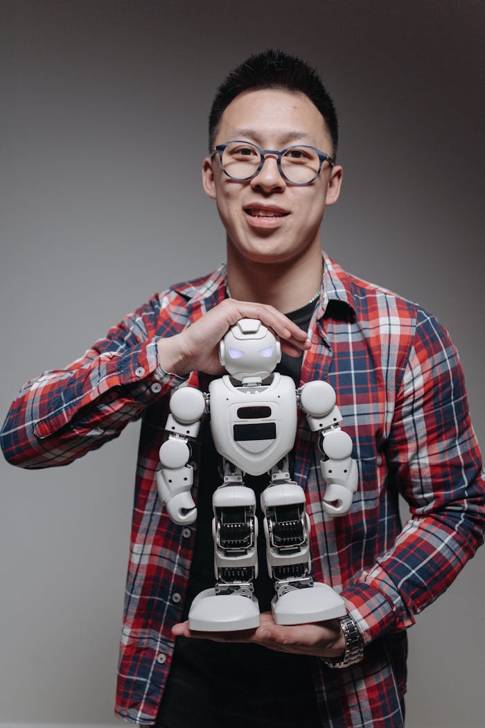 Asian man in plaid shirt with a toy robot in a studio setting.