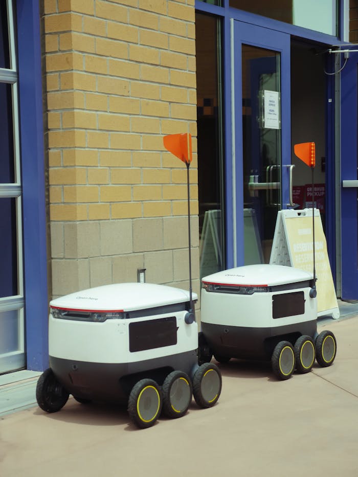 about-bg Two modern delivery robots wait outside a building, showcasing advances in technology.